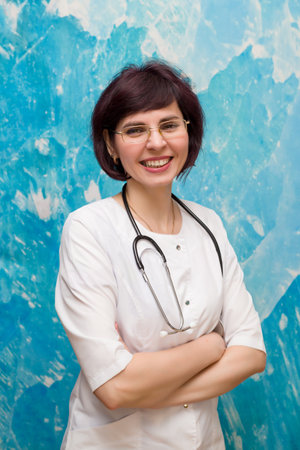 Cheerful nurse in glasses stands near a blue wall.の写真素材