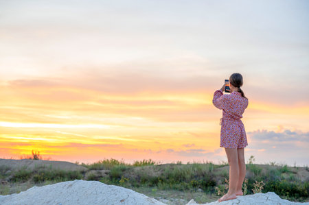teenage girl photographs the sunset on a mobile phone, recreation and entertainment for children in nature.の写真素材