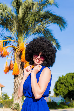 Woman with lush black curly hair in blue dress near a palm tree and the sky.の写真素材
