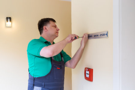 A worker screws on a sign with room numbers in a hotel.の写真素材