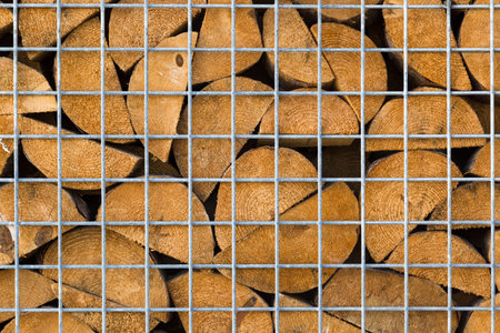 Wooden firewood logs are stacked behind a metal mesh. Wood texture and metal lattice.の写真素材