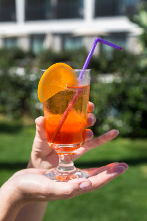 Orange cocktail with drinking straw woman hand, close-up.の写真素材