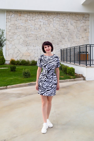 A brunette woman in a white dress with black streaks, with belt her waist near a building.の写真素材