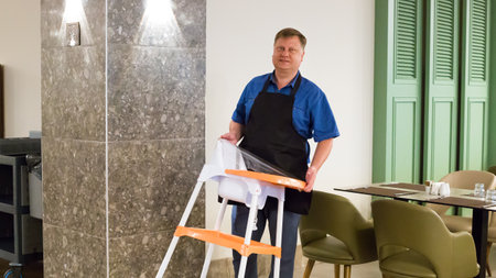 A waiter in a restaurant carries a high chair for feeding small children.の写真素材
