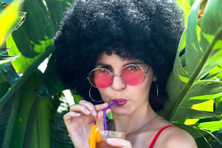Bright brunette with black curly hair with glass of cocktail tropical plants.