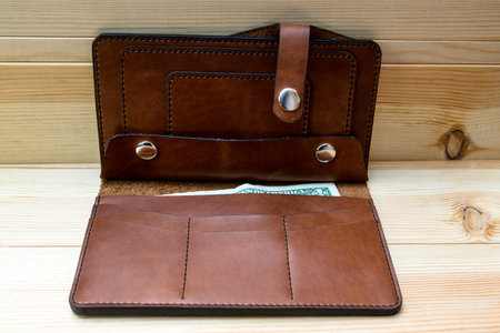 Men's wallet made of rough brown leather on a light wood background. stylish accessory for men, made...