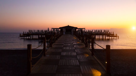 Early dark morning over the sea, the pier is barely lit by the first rays of the sun and electric lamps.の写真素材