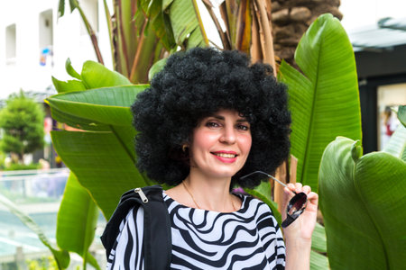 Portrait woman with lush curly hair near a large green bush city.