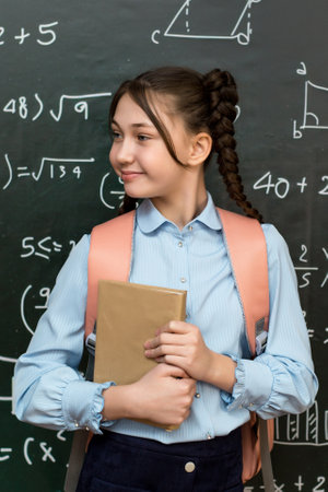 Teenage Girl with School Bag Standing at the Blackboard. Portrait of a schoolgirl 10 years old.