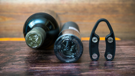 An electric corkscrew, a bottle of wine and a bottle opener lie on a dark wood background.の写真素材