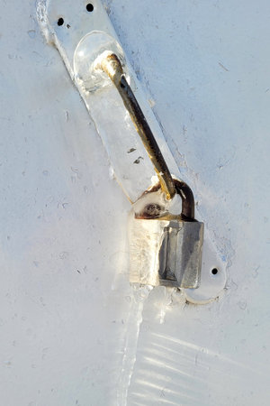 External padlock on the front door under thick layer of ice, winter ice icicle on the lock.