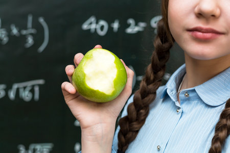 Sweet lesson: Girl with an apple - a symbol of health and education against the backdrop school blackboard.の写真素材