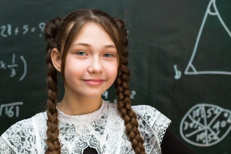 Portrait of a cute teenage girl in school clothes against the background of a chalkboard.