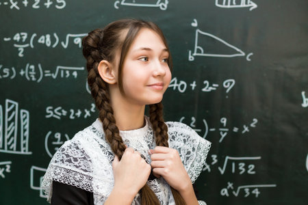 Beautiful teenage schoolgirl with brown hair near blackboard, close-up portrait.