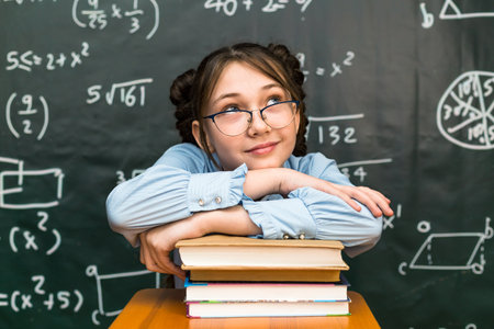 A schoolgirl girl put her hands and head on a stack of books school class.