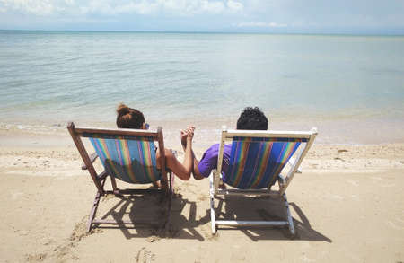 Man and Woman sit on beach chair, couple of hands against the sea viewの写真素材