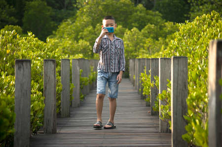 Asian boy walking and take photo on wooden bridgeの写真素材