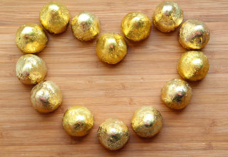A love heart shape made of gold and silver coloured chocolates against a neutral wooden backgroundの写真素材