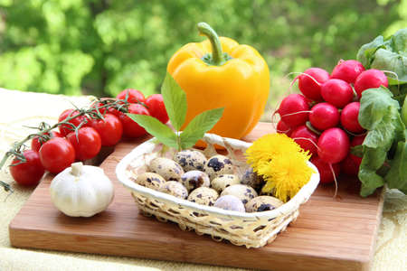 A composition of quail eggs decorated with dandelion flowers and a leaf and fresh vegetables  pepper, garlic, radish and cherry tomatoes  on wood の写真素材