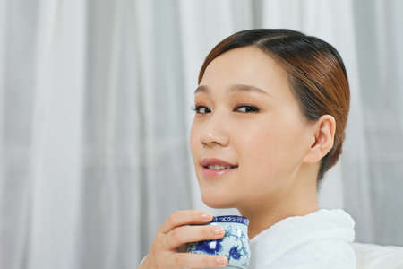 	A young woman with a bathrobe enjoying tea	