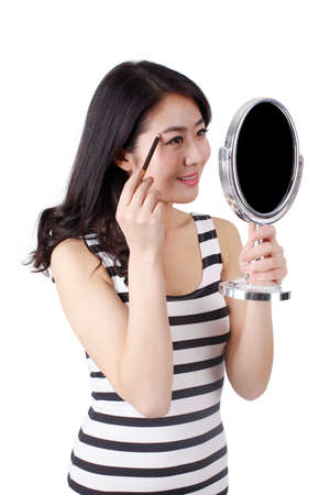 Young woman in a striped dress looking into a mirror,applying make-upの写真素材