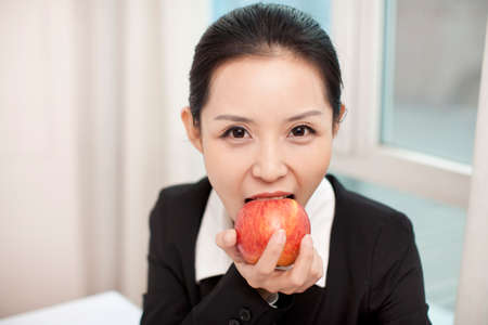 Businesswoman in her office eating an red appleの写真素材