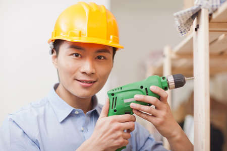 Portrait of young workman using electric drill in office,close-up