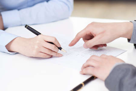 Businesswoman signing document, businessman pointing, at a desk in the office