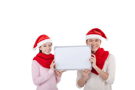 Portrait of a young couple wearing Santa hats, holding a whiteboard