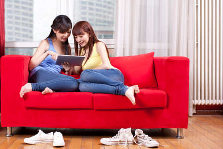 Portrait of two female friends holding computer notepad at homeの写真素材