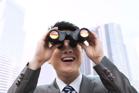 Businessman looking through a hand-held telescope, smilingの写真素材