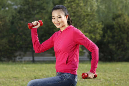 The young woman doing exercise with dumbbell in the outdoors