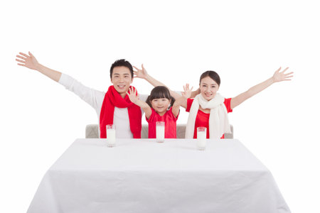 Portrait of daughter with parents opening arms,sitting at desk,with three cup of milkの写真素材