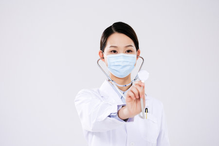 A woman doctor wearing a mask uses a stethoscope front viewの写真素材