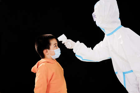 The woman doctor in medical protective clothing took the boys temperature face to face