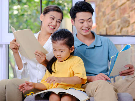 A happy family of three reading on the sofa high quality photoの写真素材