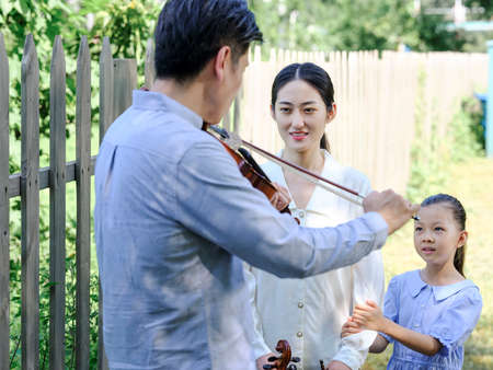 Happy family of three playing violin in the park high quality photoの写真素材