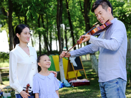 Happy family of three playing violin in the park high quality photoの写真素材