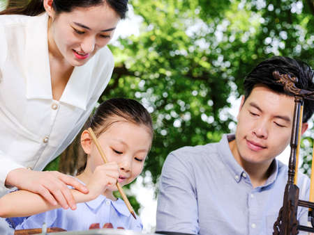 Happy family of three writing calligraphy outdoors high quality photoの写真素材