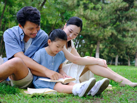 A happy family of three is reading outdoors high quality photoの写真素材