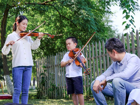 Happy family of three playing violin in the park high quality photoの写真素材