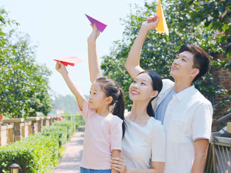 A happy family of three throwing paper airplanes outdoors high quality photoの写真素材