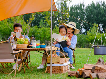 A happy family of three reading outside high quality photoの写真素材