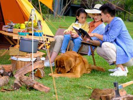 Happy family of three and pet dog reading outside high quality photoの写真素材