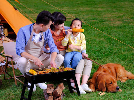 Happy family of three and pet dog barbecue in the park high quality photoの写真素材