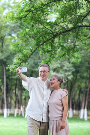 Happy old couple take selfie with mobile phone in park high quality photoの写真素材