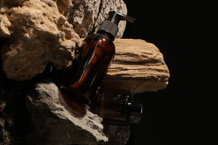 Brown glass bottle with liquid soap on a piece of wood on a black background