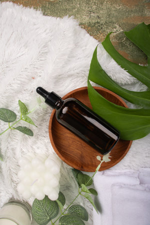 Spa and wellness setting with glass bottle of essential oil, towel, candle and green leavesの写真素材