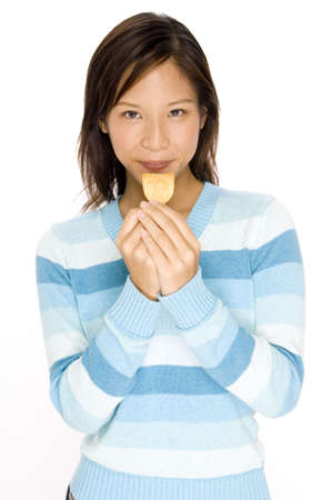 A pretty young asian woman holds a chip ready to eatの写真素材
