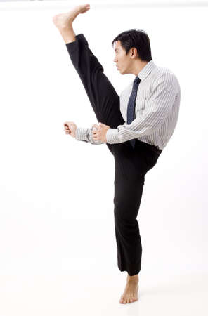 A young asian businessman in corporate dress does a high karate kickの写真素材